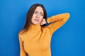 Young brunette woman standing over blue background suffering of neck ache injury, touching neck with hand, muscular pain Royalty Free Stock Photo