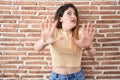 Young brunette woman standing over bricks wall afraid and terrified with fear expression stop gesture with hands, shouting in Royalty Free Stock Photo