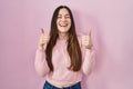 Young brunette woman standing over pink background success sign doing positive gesture with hand, thumbs up smiling and happy Royalty Free Stock Photo