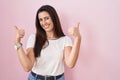 Young brunette woman standing over pink background success sign doing positive gesture with hand, thumbs up smiling and happy Royalty Free Stock Photo