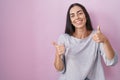 Young brunette woman standing over pink background success sign doing positive gesture with hand, thumbs up smiling and happy Royalty Free Stock Photo