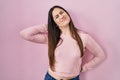 Young brunette woman standing over pink background suffering of neck ache injury, touching neck with hand, muscular pain Royalty Free Stock Photo