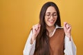 Young brunette woman standing over yellow background wearing glasses excited for success with arms raised and eyes closed Royalty Free Stock Photo