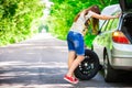 Young brunette woman stands near a silver car on the roadside with a broken wheel Royalty Free Stock Photo