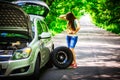 Young brunette woman stands near a silver car on the roadside with a broken wheel Royalty Free Stock Photo