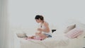 Young brunette woman stretches on a bed. Beautiful girl using laptop during breakfast. Drinking juice and dancing. Royalty Free Stock Photo