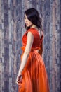 Young brunette woman in stylish orange silk dress posing on wood