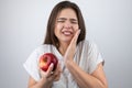 Young brunette woman suffering toothache holding red apple in her hand standing on isolated white background healthcare