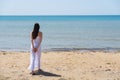 Young brunette woman in summer white dress standing on beach and looking to the sea. Royalty Free Stock Photo