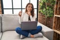 Young brunette woman using laptop holding keys of new home serious face thinking about question with hand on chin, thoughtful Royalty Free Stock Photo