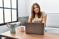 Young brunette woman using laptop at home drinking a cup of coffee with hand on stomach because indigestion, painful illness