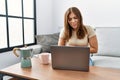 Young brunette woman using laptop at home drinking a cup of coffee with hand on stomach because nausea, painful disease feeling