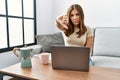 Young brunette woman using laptop at home drinking a cup of coffee looking unhappy and angry showing rejection and negative with Royalty Free Stock Photo