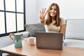 Young brunette woman using laptop at home drinking a cup of coffee showing and pointing up with fingers number four while smiling Royalty Free Stock Photo