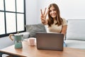 Young brunette woman using laptop at home drinking a cup of coffee showing and pointing up with fingers number three while smiling Royalty Free Stock Photo