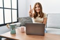 Young brunette woman using laptop at home drinking a cup of coffee showing and pointing up with fingers number two while smiling Royalty Free Stock Photo