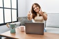 Young brunette woman using laptop at home drinking a cup of coffee success sign doing positive gesture with hand, thumbs up Royalty Free Stock Photo