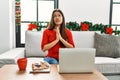 Young brunette woman using laptop sitting on the sofa on christmas begging and praying with hands together with hope expression on Royalty Free Stock Photo