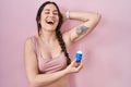 Young brunette woman using roll on deodorant smiling and laughing hard out loud because funny crazy joke Royalty Free Stock Photo