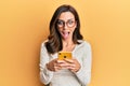 Young brunette woman using smartphone over yellow background celebrating crazy and amazed for success with open eyes screaming Royalty Free Stock Photo