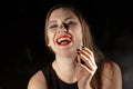 Young brunette woman vaping e-cigarette with smoke on dark background, laughing, drunk. Red lipstick, smoky eyes, black manicure,