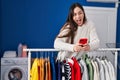 Young brunette woman waiting for laundry using smartphone celebrating crazy and amazed for success with open eyes screaming Royalty Free Stock Photo