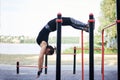 Young brunette woman, wearing black fitness overall, doing stretching exercises, hanging on horizontal bars on sports playground