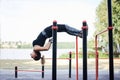 Young brunette woman, wearing black fitness overall, doing stretching exercises, hanging on horizontal bars on sports playground