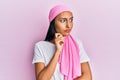 Young brunette woman wearing breast cancer support pink scarf serious face thinking about question with hand on chin, thoughtful