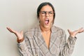 Young brunette woman wearing business jacket and glasses crazy and mad shouting and yelling with aggressive expression and arms Royalty Free Stock Photo