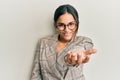 Young brunette woman wearing business jacket and glasses smiling cheerful offering palm hand giving assistance and acceptance Royalty Free Stock Photo