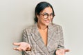 Young brunette woman wearing business jacket and glasses smiling cheerful with open arms as friendly welcome, positive and Royalty Free Stock Photo