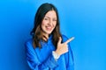 Young brunette woman wearing casual blue shirt cheerful with a smile of face pointing with hand and finger up to the side with