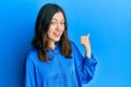 Young brunette woman wearing casual blue shirt smiling with happy face looking and pointing to the side with thumb up Royalty Free Stock Photo