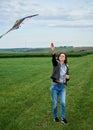 Young brunette woman, wearing casual clothes green t-shirt, playing with colorful kite on green field meadow in summer, running, Royalty Free Stock Photo
