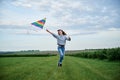 Young brunette woman, wearing casual clothes green t-shirt, playing with colorful kite on green field meadow in summer, running, Royalty Free Stock Photo