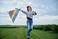 Young brunette woman, wearing casual clothes green t-shirt, playing with colorful kite on green field meadow in summer, running,