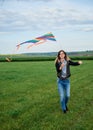 Young brunette woman, wearing casual clothes green t-shirt, playing with colorful kite on green field meadow in summer, running, Royalty Free Stock Photo