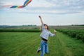 Young brunette woman, wearing casual clothes green t-shirt, playing with colorful kite on green field meadow in summer, running, Royalty Free Stock Photo
