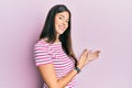 Young brunette woman wearing casual clothes over pink background inviting to enter smiling natural with open hand