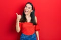 Young brunette woman wearing casual red shirt pointing thumb up to the side smiling happy with open mouth Royalty Free Stock Photo