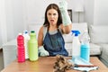 Young brunette woman wearing cleaner apron and gloves cleaning at home angry and mad raising fist frustrated and furious while