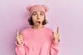 Young brunette woman wearing cute wool cap amazed and surprised looking up and pointing with fingers and raised arms Royalty Free Stock Photo