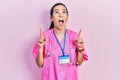Young brunette woman wearing doctor uniform and stethoscope amazed and surprised looking up and pointing with fingers and raised Royalty Free Stock Photo