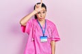 Young brunette woman wearing doctor uniform and stethoscope making fun of people with fingers on forehead doing loser gesture Royalty Free Stock Photo