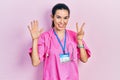 Young brunette woman wearing doctor uniform and stethoscope showing and pointing up with fingers number seven while smiling Royalty Free Stock Photo