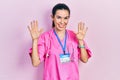 Young brunette woman wearing doctor uniform and stethoscope showing and pointing up with fingers number ten while smiling Royalty Free Stock Photo