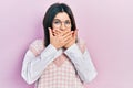 Young brunette woman wearing elegant sweater and glasses shocked covering mouth with hands for mistake