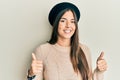 Young brunette woman wearing french look with beret success sign doing positive gesture with hand, thumbs up smiling and happy Royalty Free Stock Photo