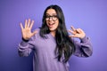 Young brunette woman wearing glasses over purple isolated background showing and pointing up with fingers number eight while